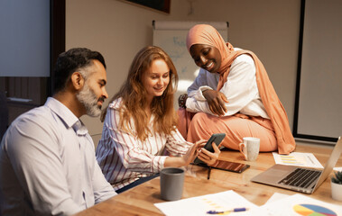 Happy diverse coworkers having discussion in modern office with mobile phone and documents at