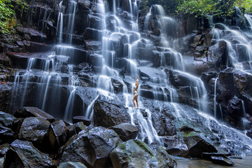 A young woman in a swimming suit at Nungnung waterfall in lush tropical forest, Bali, Indonesia