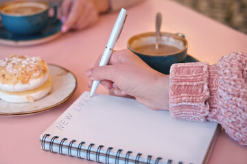 Woman Writing Plan in a Notepad Sitting on a Pink Cafe Table with Coffee Cup and Dessert. Hand...
