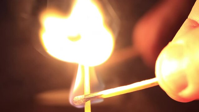 Closeup of a match ignited by another match, warm flame reflecting in glass.