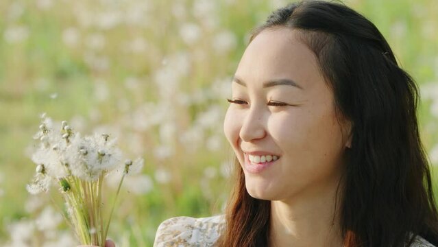 Young adult Asian woman blowing on dandelions