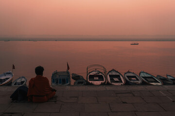 Sadu meditating in orange clothes during dawn on sacred river Ganges in Varanasi, India - obrazy, fototapety, plakaty