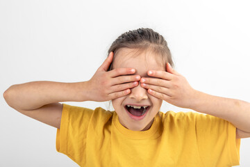 A little girl closes her eyes with her hands on a white background isolated.