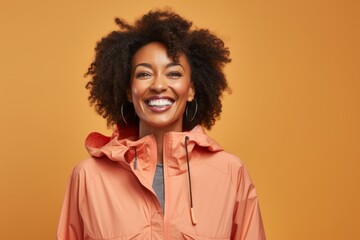 Obraz na płótnie Canvas Portrait of a jovial afro-american woman in her 40s wearing a lightweight packable anorak against a pastel orange background. AI Generation