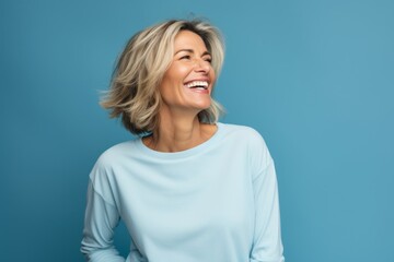 Obraz premium Portrait of a joyful woman in her 40s sporting a long-sleeved thermal undershirt against a soft blue background. AI Generation