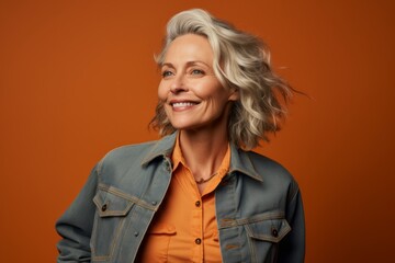 Obraz na płótnie Canvas Portrait of a satisfied woman in her 50s sporting a rugged denim jacket against a soft orange background. AI Generation