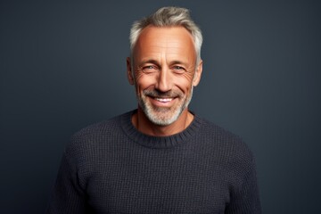 Obraz premium Portrait of a grinning man in his 50s wearing a cozy sweater against a soft gray background. AI Generation