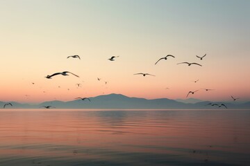  a flock of seagulls flying over a body of water with a mountain range in the distance in the distance in the distance is a body of water with birds flying in the foreground.