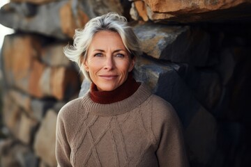 Portrait of a content woman in her 60s wearing a thermal fleece pullover against a rocky cliff...