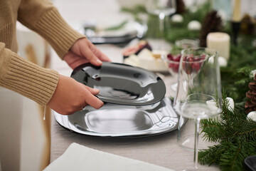 Closeup of unknown caucasian woman placing empty plates for guests on Christmas table