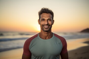 Portrait of a glad indian man in his 30s wearing a moisture-wicking running shirt against a stunning sunset beach background. AI Generation