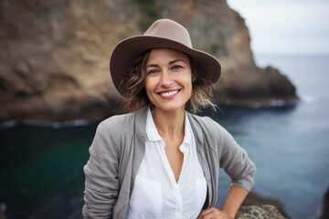 Portrait of a joyful woman in her 40s donning a classic fedora against a spectacular sea cave background. AI Generation - obrazy, fototapety, plakaty