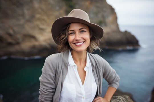 Portrait of a joyful woman in her 40s donning a classic fedora against a spectacular sea cave background. AI Generation
