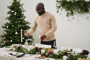 Medium full shot of smiling african american man placing wineglass on christmas festive table