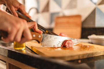 Person cutting sausage on a board. Barbecue. Closeup on hand.