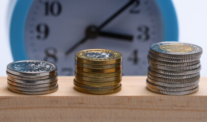Wykres słupkowy ułożony z pieniędzy, polskich monet, w tle zegar odmierzający czas