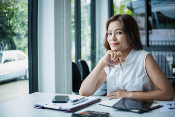 Businesswoman sitting at desk on couch in workplace or at home working on laptop and analyzing data on charts and graphs and writing on papers 