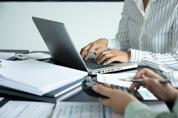 Fototapeta premium Businesswoman sitting at desk on couch in workplace or at home working on laptop and analyzing data on charts and graphs and writing on papers 