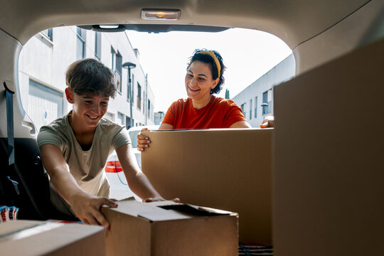 Smiling mother and son picking boxes from car during relocation