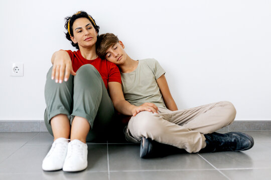 Teenager sitting on floor with mother and leaning head on mother shoulder