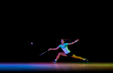 Badminton athlete demonstrates her skills in attack and defense against black background in neon...