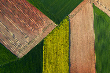 Textured aerial view of farmland showing geometric patterns of plowed fields in green, yellow, and brown tones