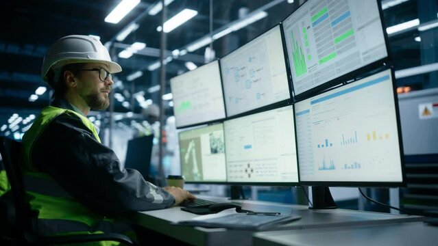 Caucasian Male Process Engineer Using Multi Monitor Workstation To Control Production Of Modern Heavy Machinery on Autonomous Assembly Line With Robotic Arms. Man Adjusting Manufacturing Processes.