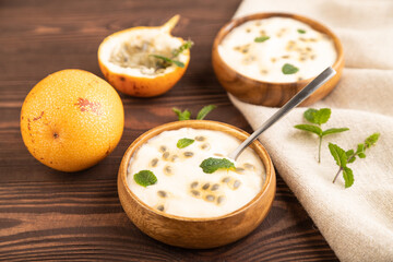 Yoghurt with granadilla and mint in wooden bowl on brown wooden, side view, selective focus.