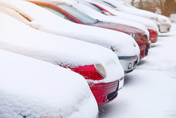 Row of parked cars covered with snow. Snow covered parking lot in winter city street. Cars standing in the snowy parking lot. Cold and snowy winter. Selective focus..