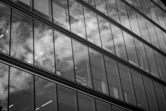 Modern office building glass facade, sky reflection in windows. Skyscrapers urban skyline. Architectural details. High rise estate black and white pic