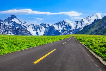 Tuinposter Asphalt highway and green meadows with snow mountain natural landscape under the blue sky © ABCDstock