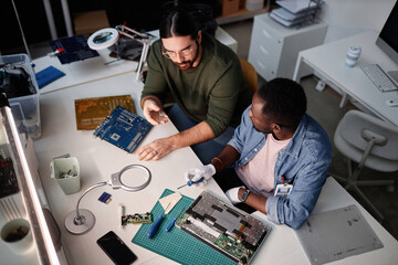 High angle portrait of two men fixing electronics in computer repair shop, copy space