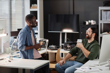 Side view portrait of two smiling adult men chatting and drinking coffee in tech repair shop