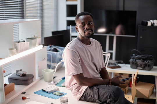 Portrait of Black adult man smiling at camera at workplace in tech repair shop, copy space