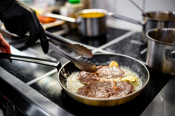 Professional chef cooking beef steak in frying pan on stove in restaurant kitchen