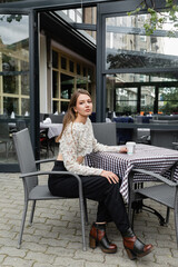 young woman sitting with paper cup on terrace of outdoor cafe and urban street in Berlin