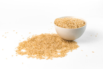 Brown rice lies in a ceramic bowl and is scattered on the table next to it