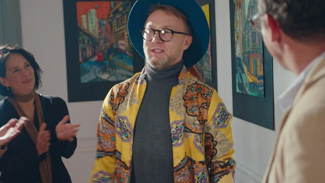 Gallery curator introducing artist to gallery visitors, he greeting people for applauds and giving speech on exhibition opening