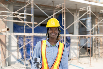 Naklejka na ściany i meble Portrait of African American female civil engineer wearing safety vest with helmet standing and hold blueprint building plan at construction site outside
