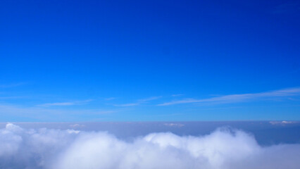 Sea of clouds view from a mountain peak against a background of a blue sky.