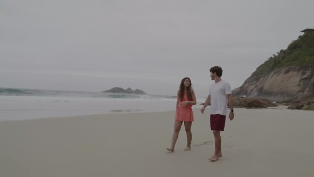 Jovem casal conversando, andando pela praia, apontando para algo. Cinematico 4k.