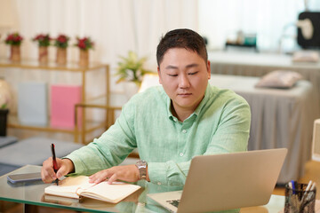 Spa salon manager checking messages from clients and writing notes in planner