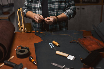 Closeup and cropped photo of craftsman threading a needle to sew a leather product for a customer....