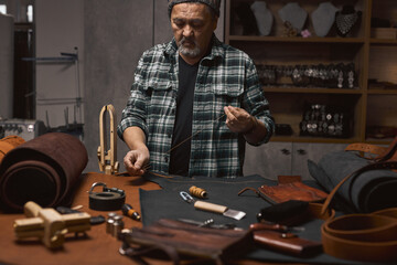 handsome bearded tailor prepares thread and needle for sewing, portrait of talented craftsman working at workshop