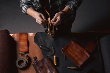 Obraz premium Working process of the leather wallet in the leather workshop. Man holding crafting tool and working. Tanner in old tannery. close up cropped top view photo.