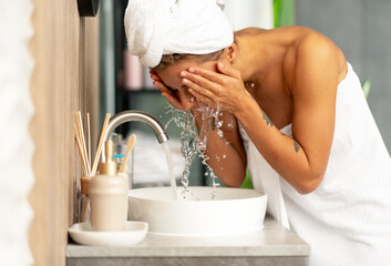 Beautiful woman wearing white towel after shower washing face with water in stylish bathroom at home - Powered by Adobe