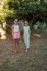 Ritratto di moda di due sorelle gemelle di nove anni in campagna con occhiali da sole e capelli legati.