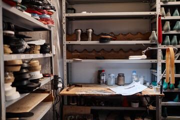 Part of workplace of professional shoemaker with small table with various supplies and shelves with workpieces for footwear