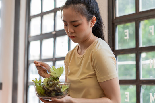 Unhappy Asian girl&nbsp;eating green vegetables salad upset bored of dieting. anorexia Bored&nbsp; Woman with unsatisfied facial emotional