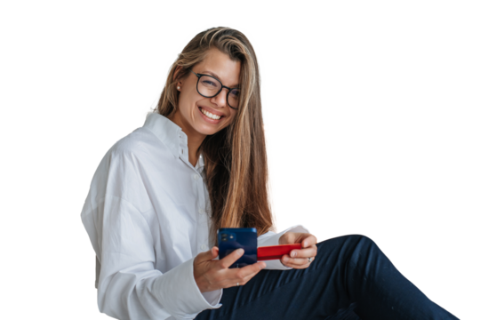 Gorgeous long haired woman in white shirt, glasses and black pants holds phone and credit card toothy smiles sitting against transparent background makes online purchase.